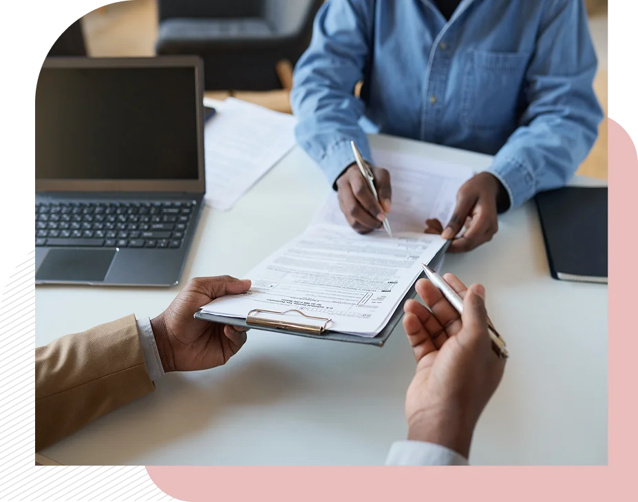 Signing documents at a desk with laptop.